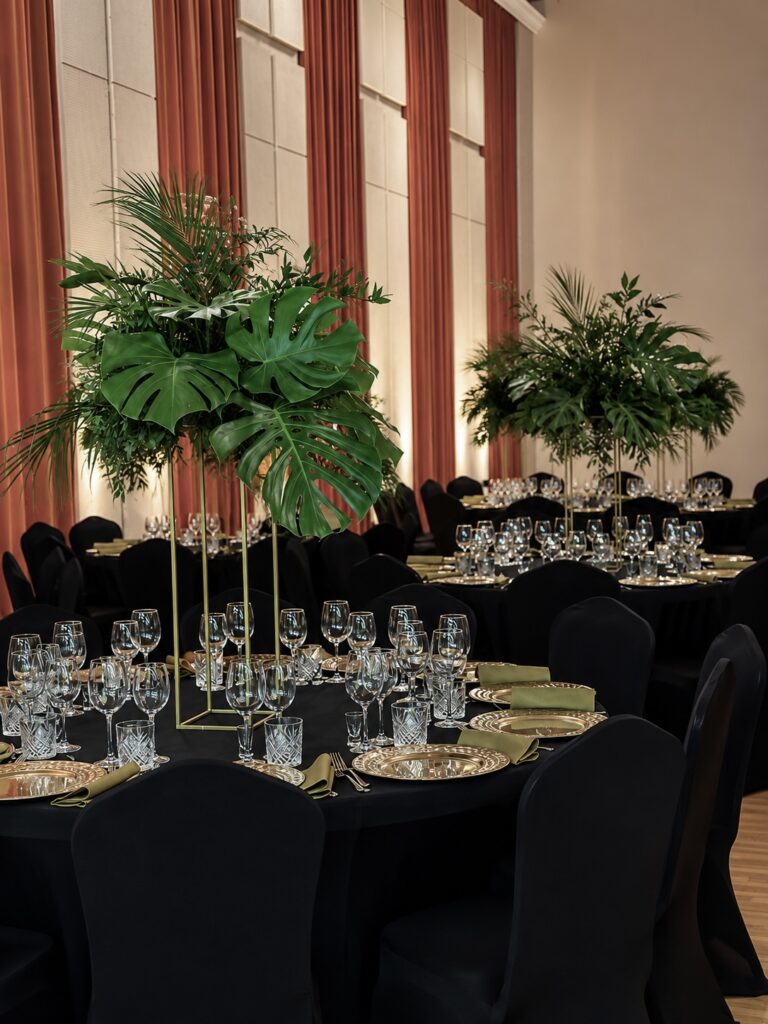Dekoracja eventu firmowego z wysokimi kompozycjami z zieleni